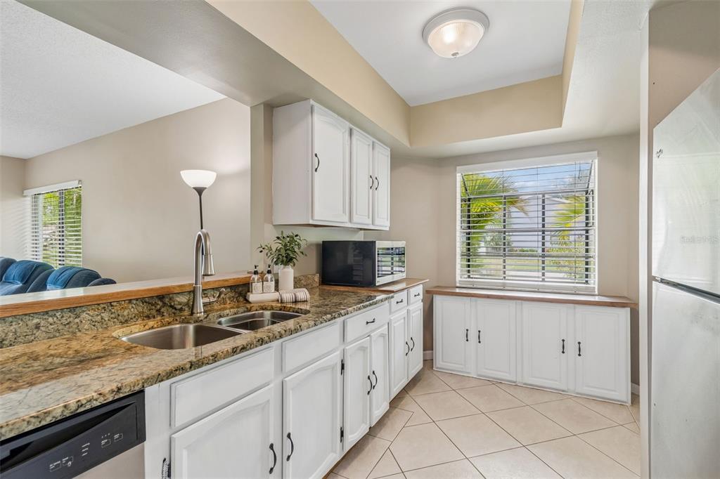 A kitchen features white cabinets, granite countertops, a double sink, and a window with blinds — 1109 SOMERSET CIRCLE S, DUNEDIN, FL