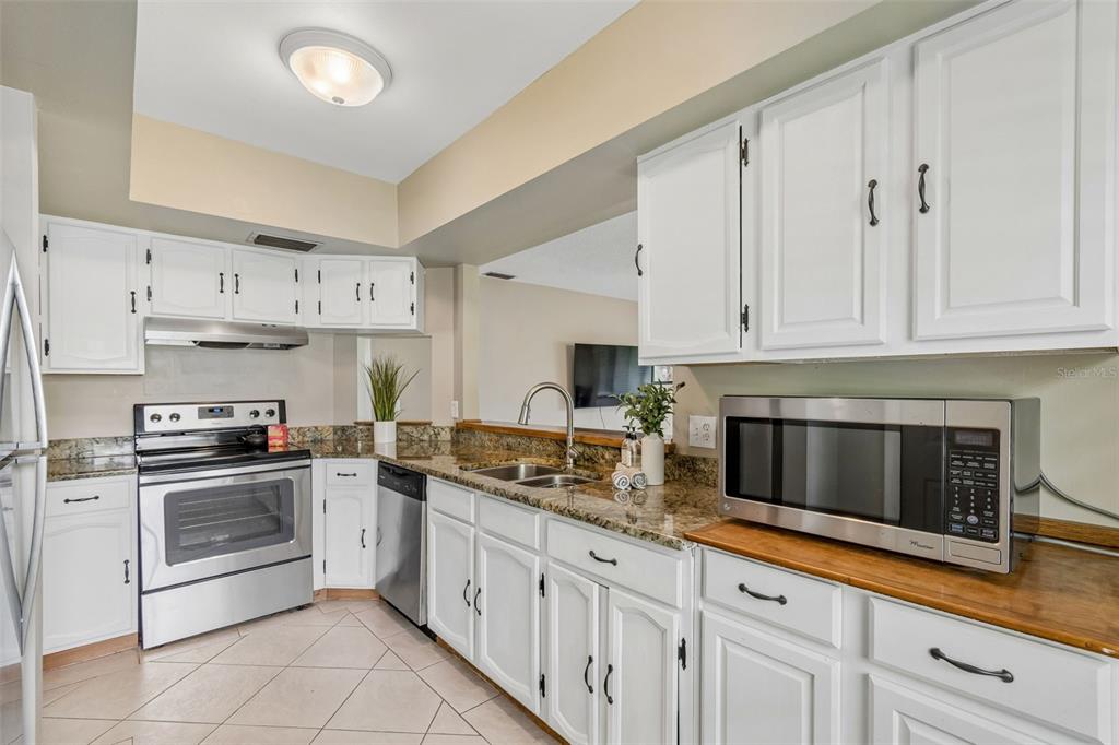 A kitchen with white cabinets, granite countertops, stainless steel appliances, and a tile floor — 1109 SOMERSET CIRCLE S, DUNEDIN, FL