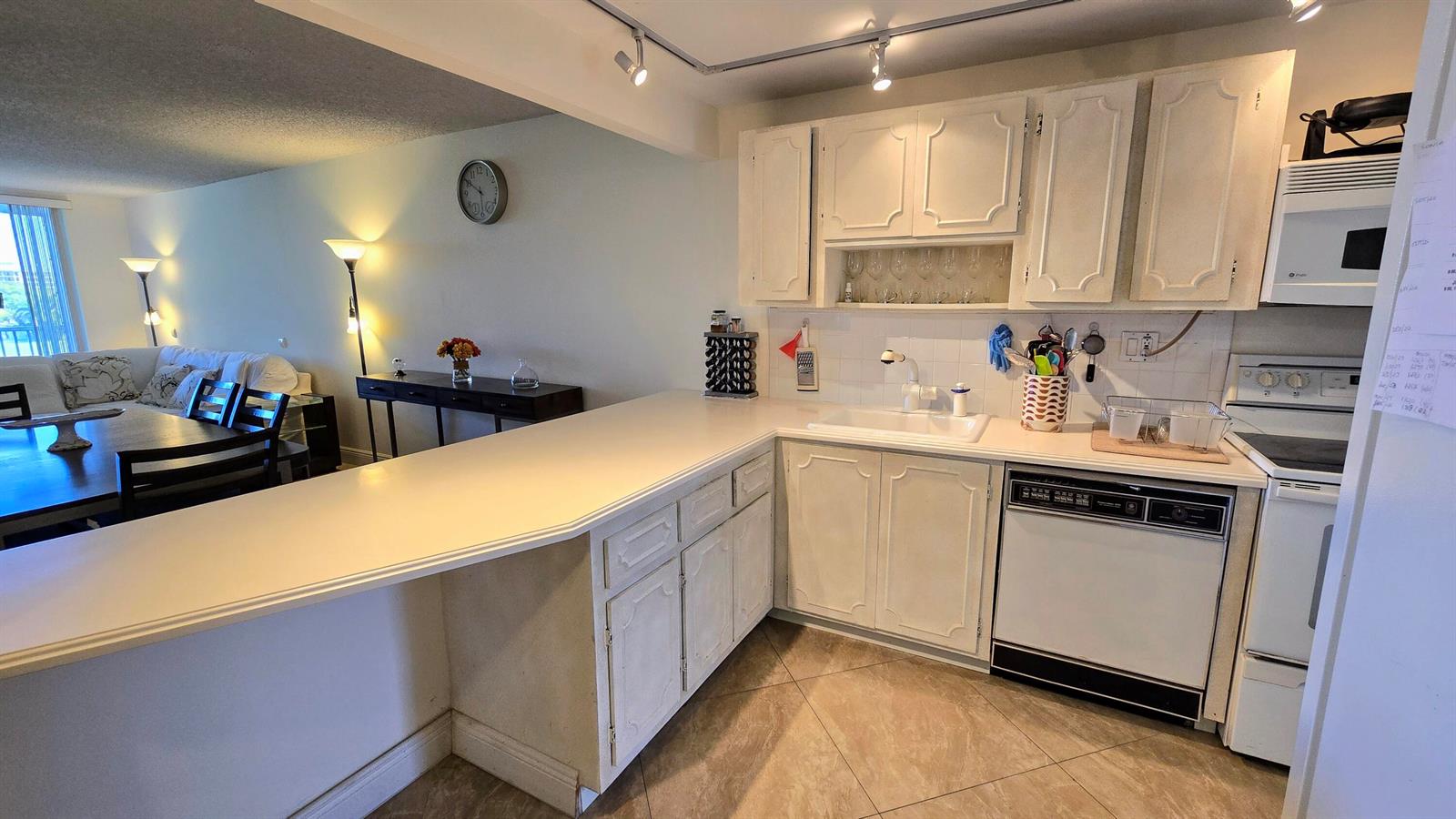 A kitchen with white cabinets, a peninsula counter, and tile flooring, open to a living area — 3100 N Course Lane # 410, Pompano Beach FL 33069, POMPANO BEACH, FL