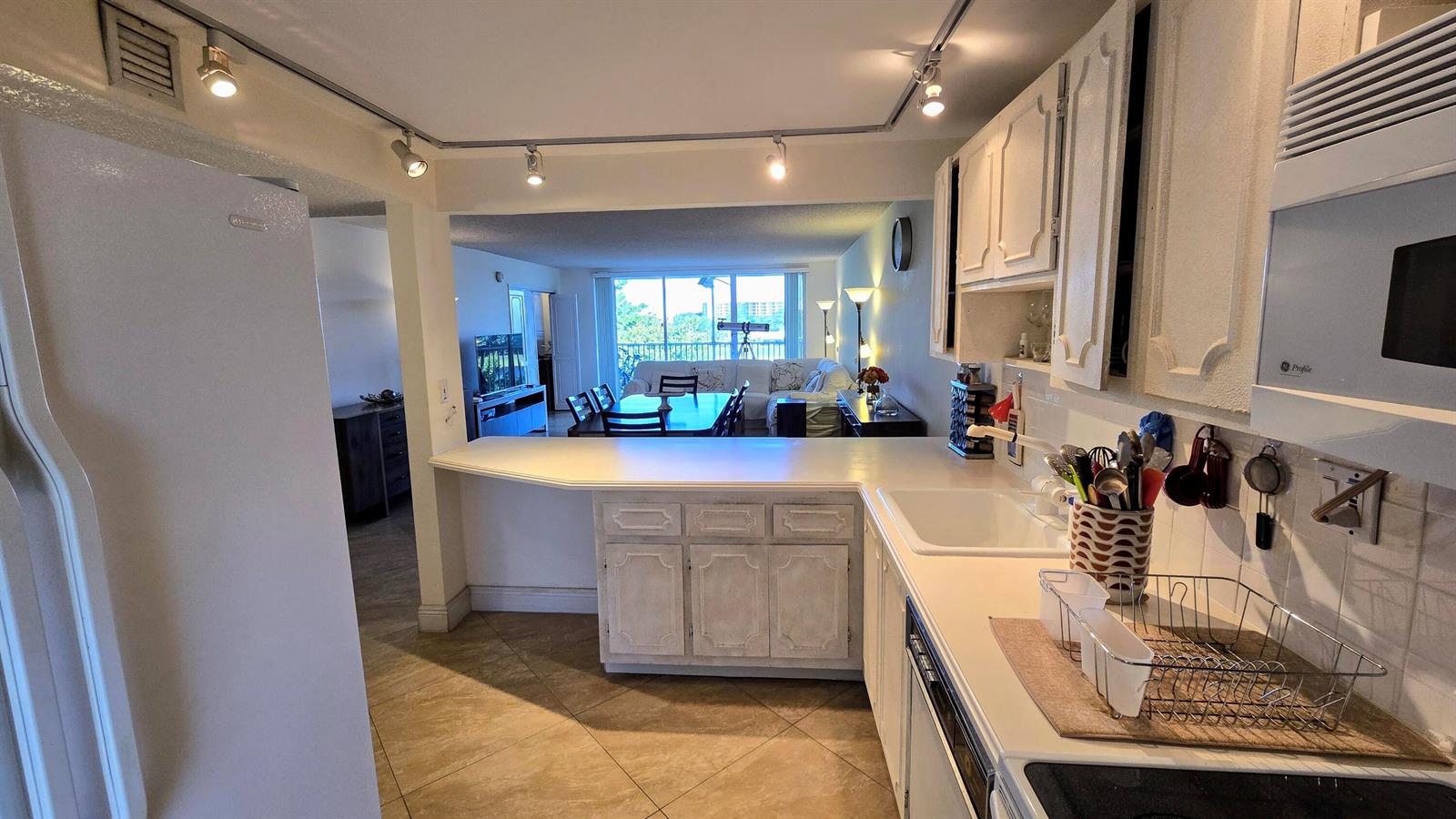 A kitchen with white cabinets and countertops overlooks a living and dining area — 3100 N Course Lane # 410, Pompano Beach FL 33069, POMPANO BEACH, FL