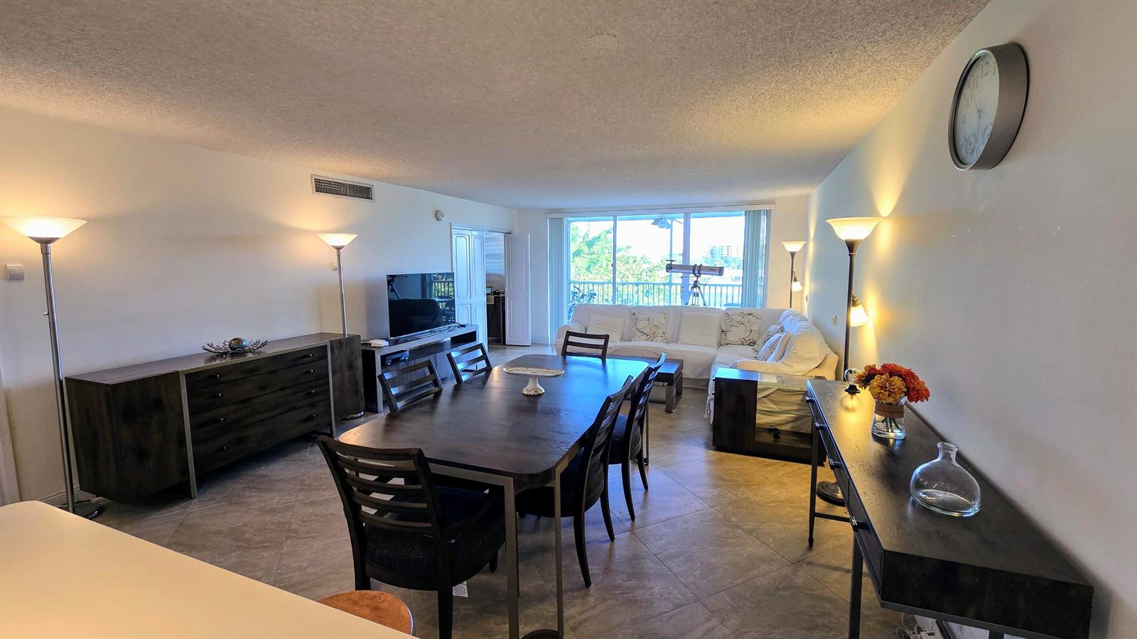 An open-concept living and dining area features tile flooring, dark wood furniture, and a balcony — 3100 N Course Lane # 410, Pompano Beach FL 33069, POMPANO BEACH, FL