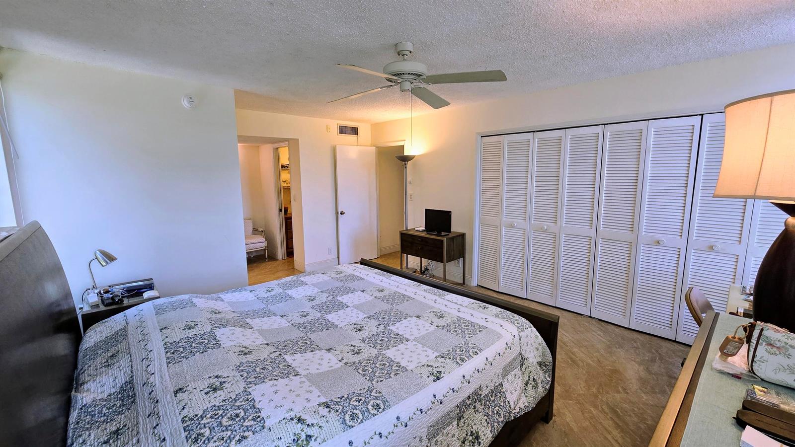 A bedroom features a bed with a patterned quilt, a ceiling fan, and louvered closet doors — 3100 N Course Lane # 410, Pompano Beach FL 33069, POMPANO BEACH, FL