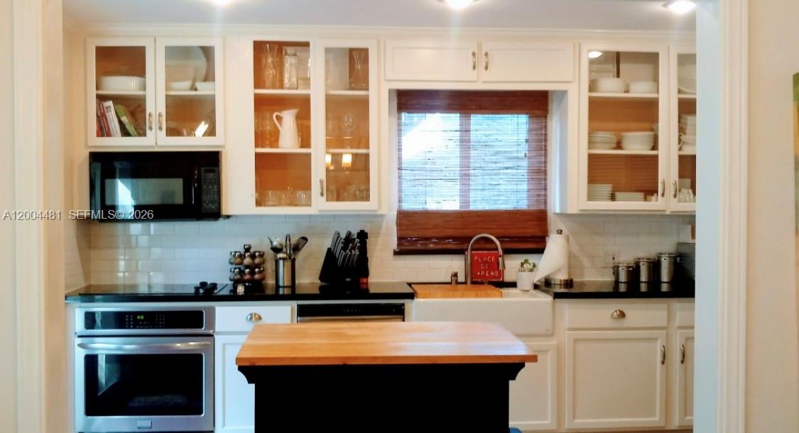 A kitchen features white cabinetry, black countertops, a farmhouse sink, and a wooden island — 5718 SW 48th St, South Miami FL 33155, SOUTH MIAMI, FL
