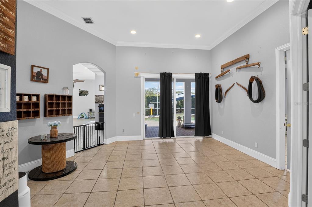A tiled room features a sliding glass door, wall-mounted vintage farm equipment, and an arched entryway — 2325 CHESTERFIELD CIRCLE, LAKELAND, FL