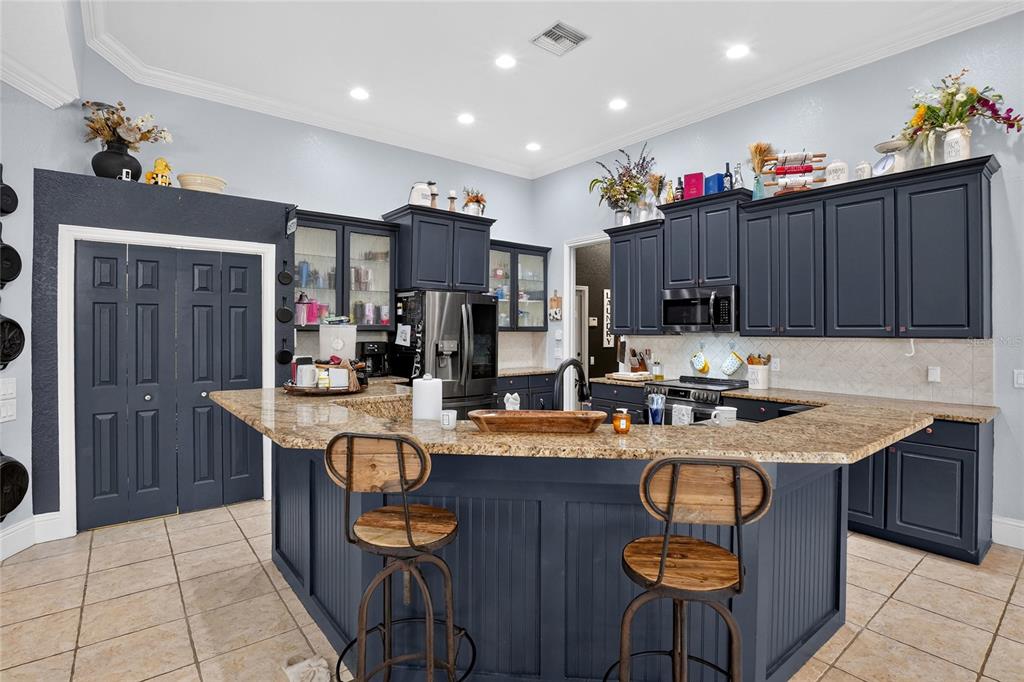 A kitchen features dark blue cabinets, granite countertops, a central island, and two wooden stools — 2325 CHESTERFIELD CIRCLE, LAKELAND, FL
