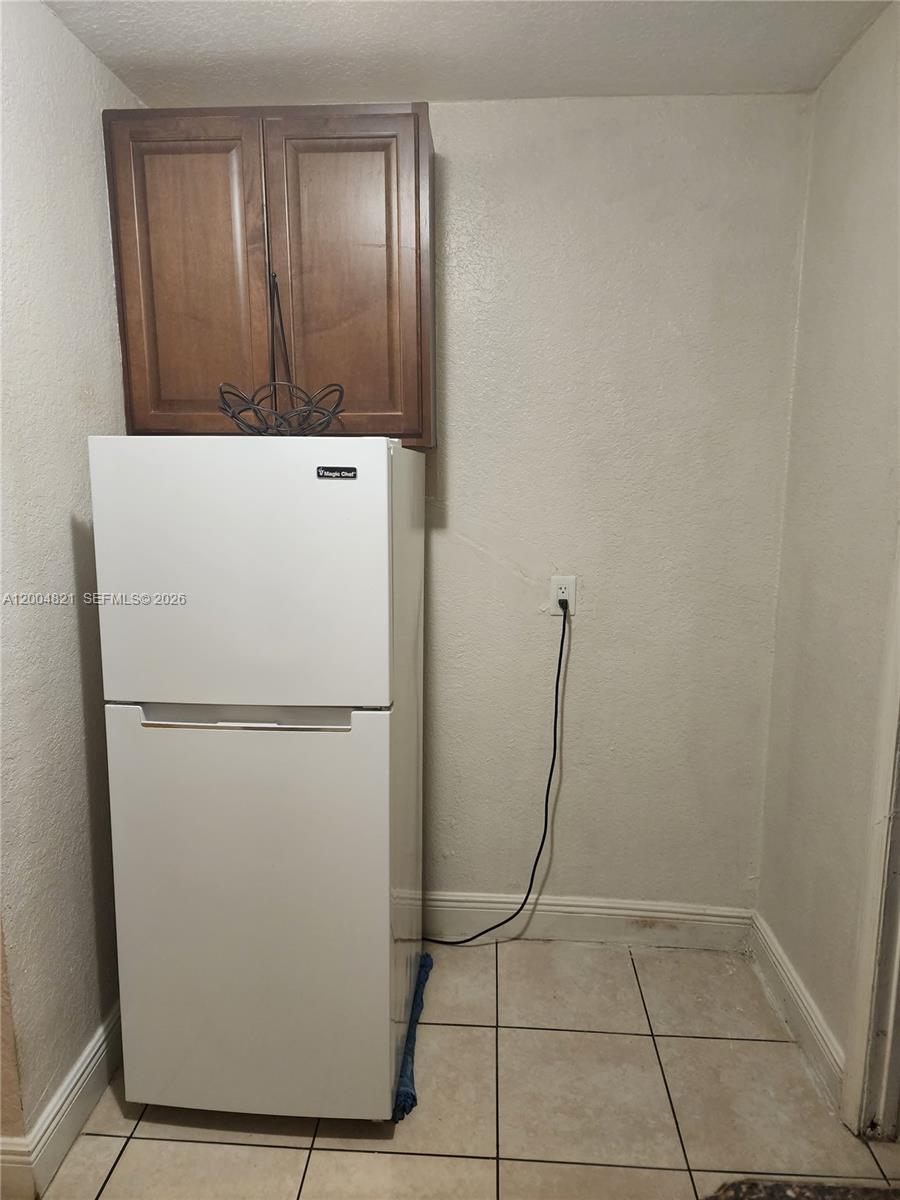 A white refrigerator sits beneath a brown wooden cabinet in a tiled kitchen corner — 6421 SW 18th St # 1, Miramar FL 33023, MIRAMAR, FL