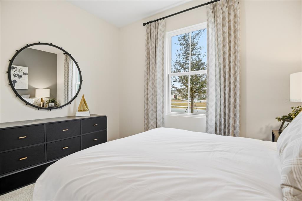 A bedroom features a black dresser, a round mirror, and a window with patterned curtains — 3236 WAGHORN DRIVE, TAVARES, FL