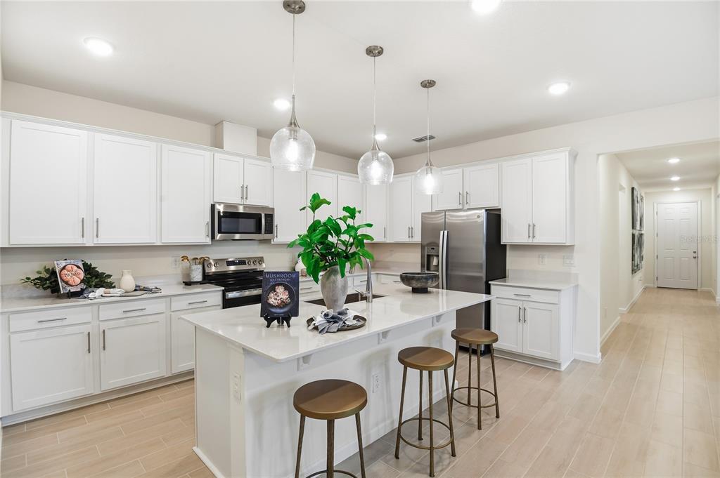 A modern kitchen features white cabinets, a central island with bar stools, and stainless appliances — 3236 WAGHORN DRIVE, TAVARES, FL