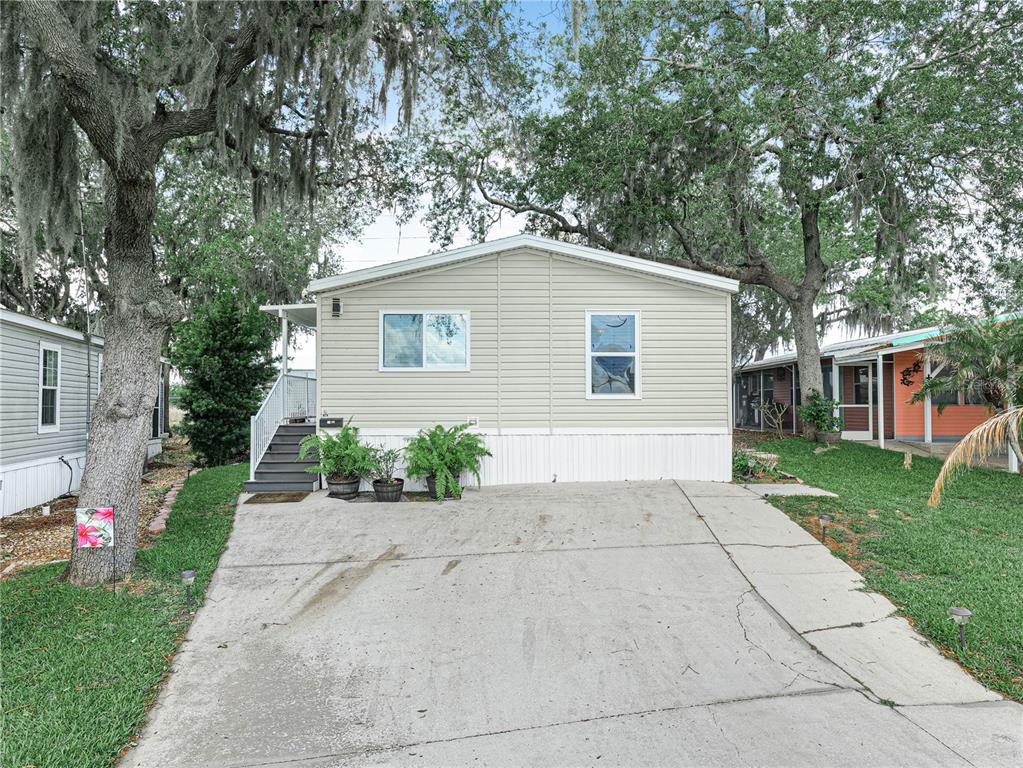 A single-story manufactured home with light siding, a concrete driveway, and large oak trees — 24 SILVERSIDES STREET, LAKE WALES, FL