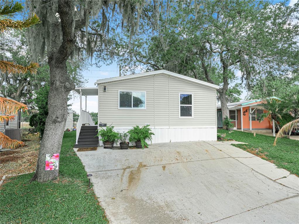 A light-colored mobile home with a concrete driveway, front steps, and surrounding trees — 24 SILVERSIDES STREET, LAKE WALES, FL