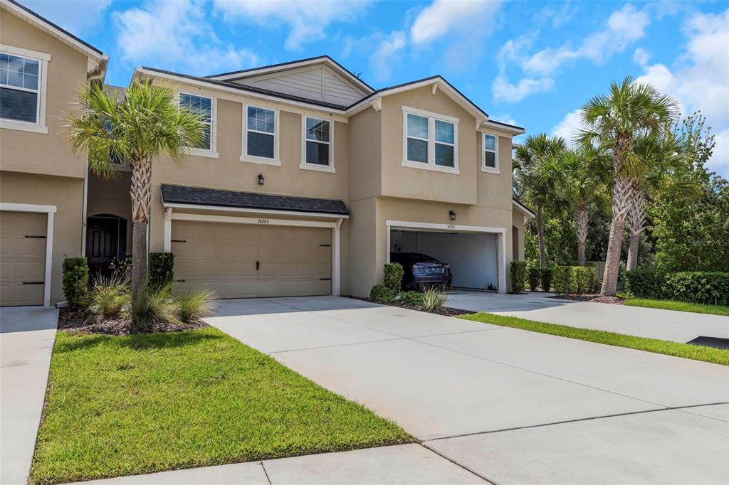 A two-story townhouse with a tan stucco exterior, two garages, and palm trees in front — 14203 DAMSELFLY DRIVE, TAMPA, FL
