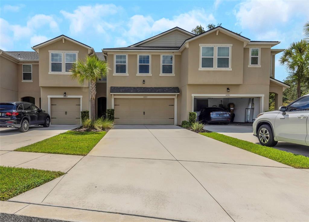 A multi-unit residential building with beige stucco siding, three garage doors, and concrete driveways — 14203 DAMSELFLY DRIVE, TAMPA, FL