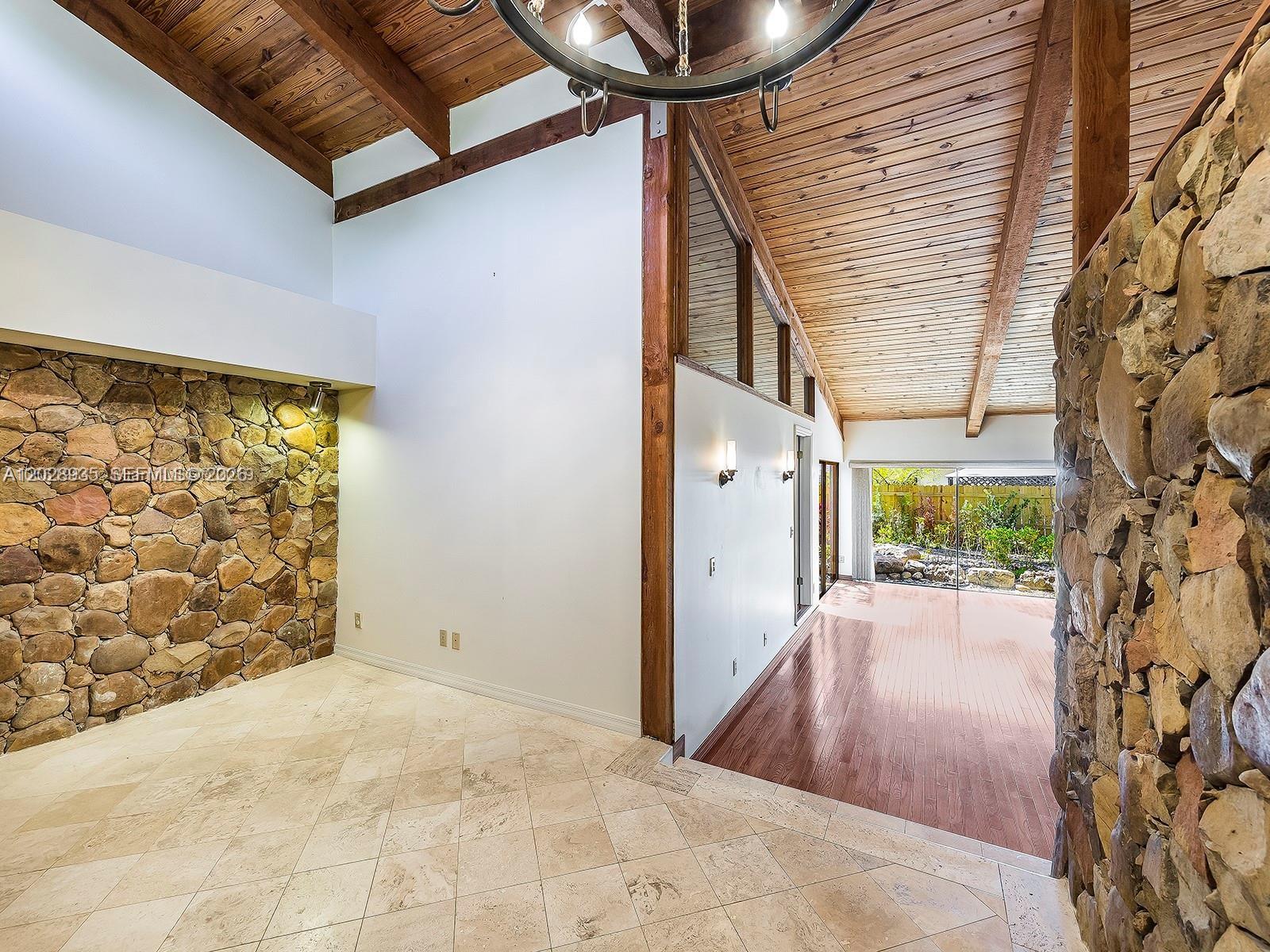 A room with a stone wall, tile flooring, and a wooden ceiling leads to a sunroom — 9055 SW 78th Ct, Miami FL 33156, MIAMI, FL