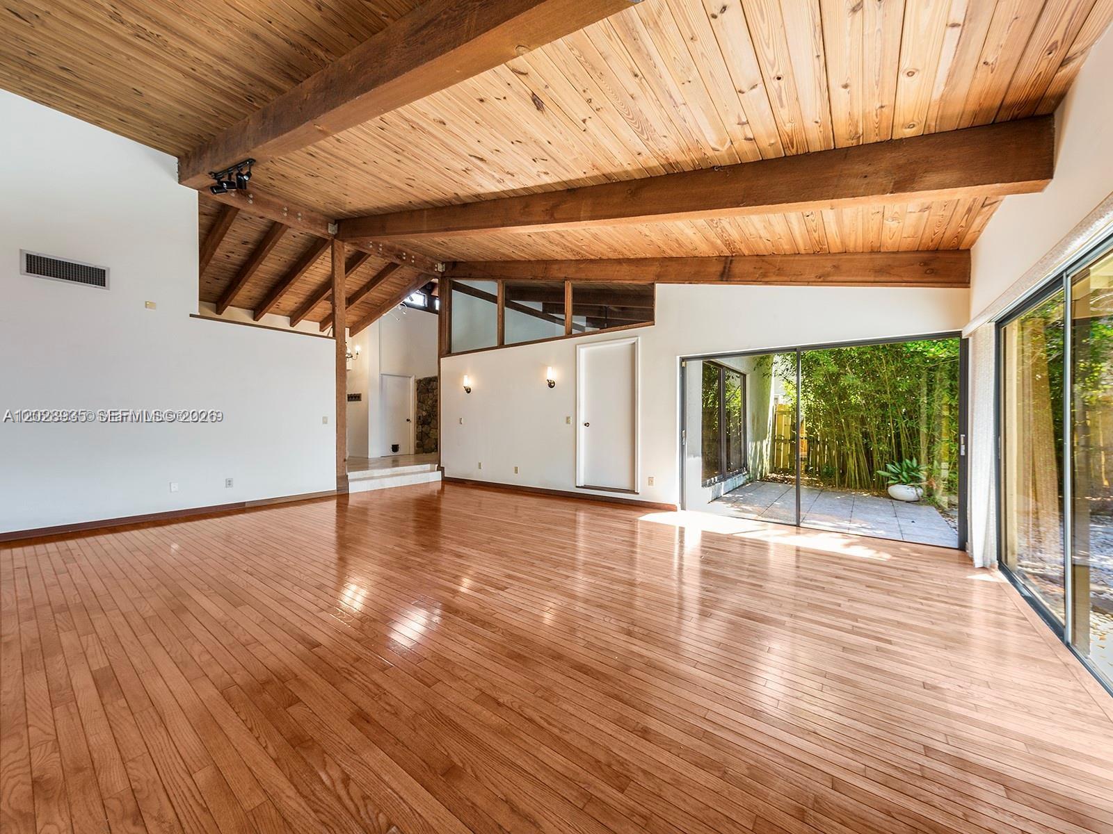 A spacious living room features hardwood floors, a vaulted wood-plank ceiling, and large sliding glass doors — 9055 SW 78th Ct, Miami FL 33156, MIAMI, FL