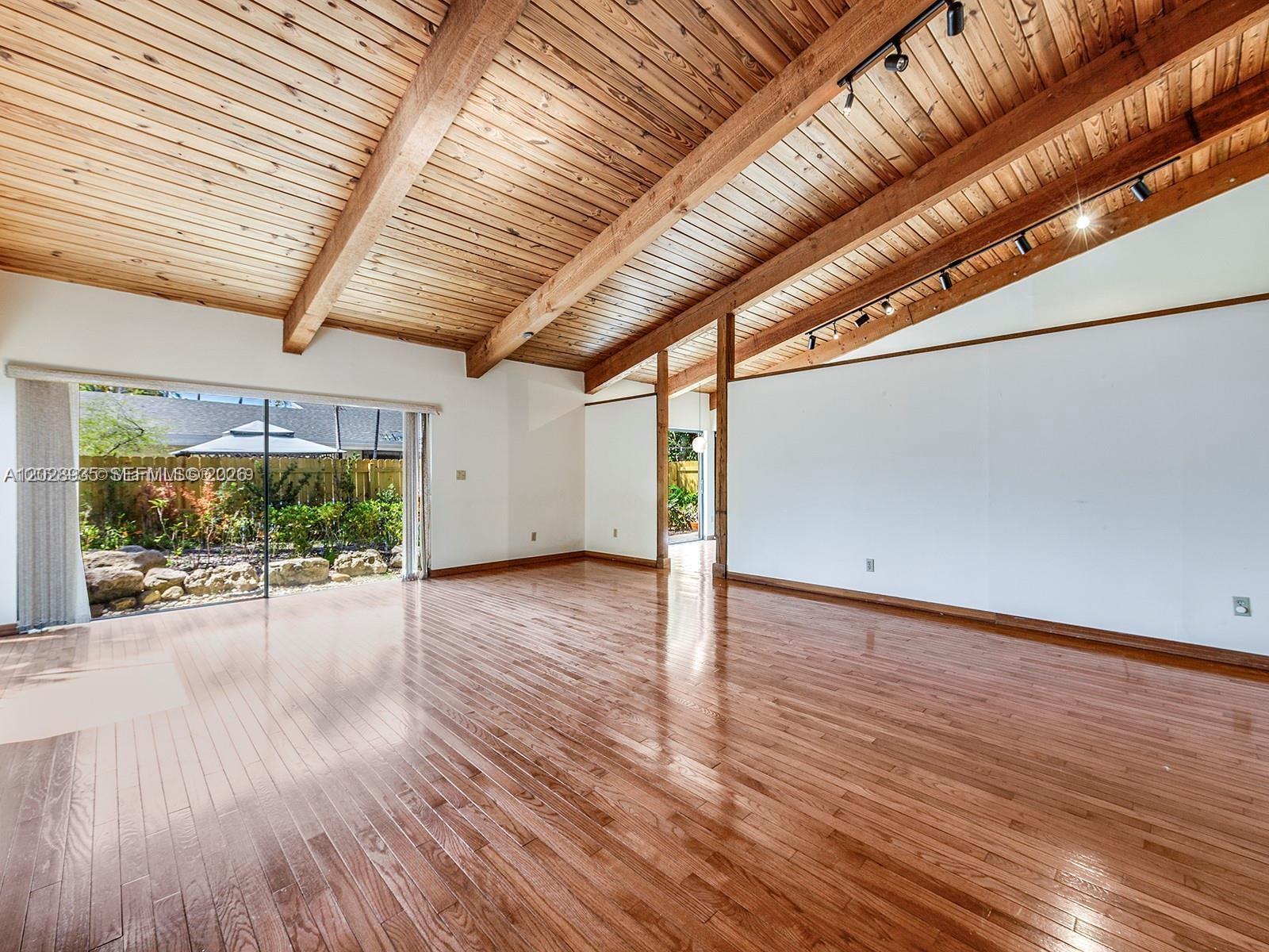 An empty living room features a vaulted wood-plank ceiling, exposed beams, and hardwood flooring — 9055 SW 78th Ct, Miami FL 33156, MIAMI, FL