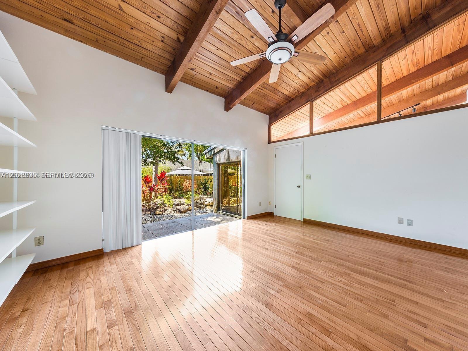 An empty room features hardwood floors, a vaulted wood-paneled ceiling, and sliding glass patio doors — 9055 SW 78th Ct, Miami FL 33156, MIAMI, FL