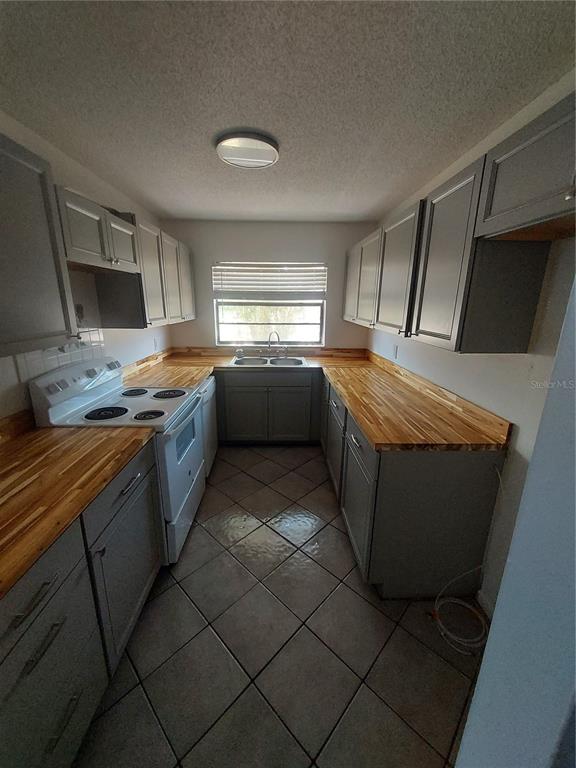 A galley kitchen features gray cabinets, butcher block countertops, and diagonal tile flooring — 3535 E FORT KING STREET UNIT 160, OCALA, FL