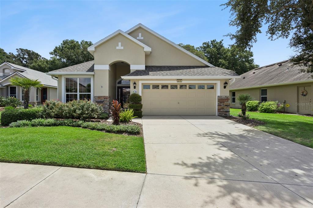 A single-story suburban house with a beige stucco exterior, stone accents, and a two-car garage — 8270 BRIDGEPORT BAY CIRCLE, MOUNT DORA, FL