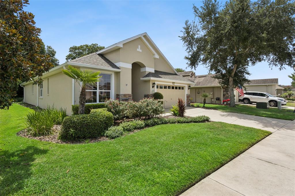 A single-story beige house with a two-car garage, stone accents, and a manicured lawn — 8270 BRIDGEPORT BAY CIRCLE, MOUNT DORA, FL