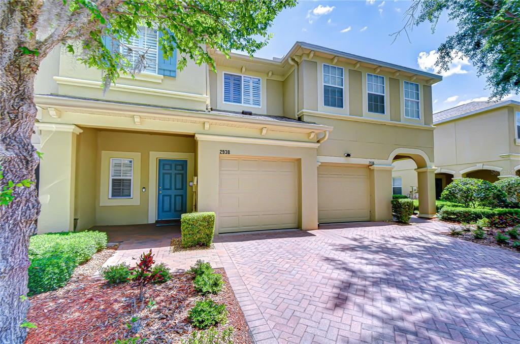 A two-story tan townhouse with a blue front door and a brick paver driveway — 2938 LOCHCARRON DRIVE, LAND O LAKES, FL