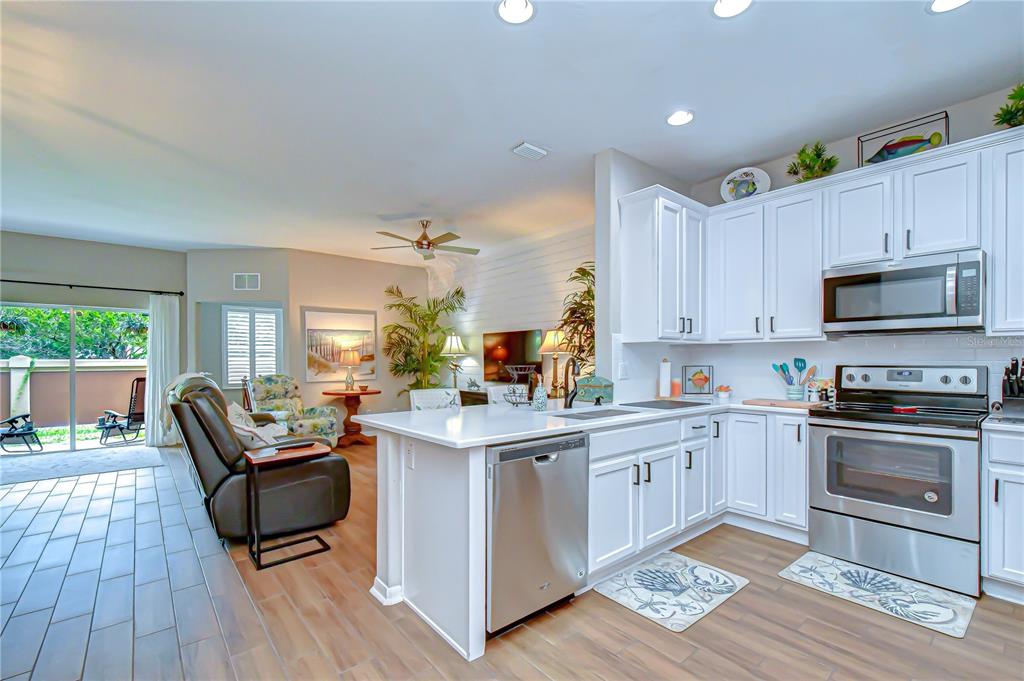 A kitchen with white cabinets and a stainless steel dishwasher opens to a living area — 2938 LOCHCARRON DRIVE, LAND O LAKES, FL