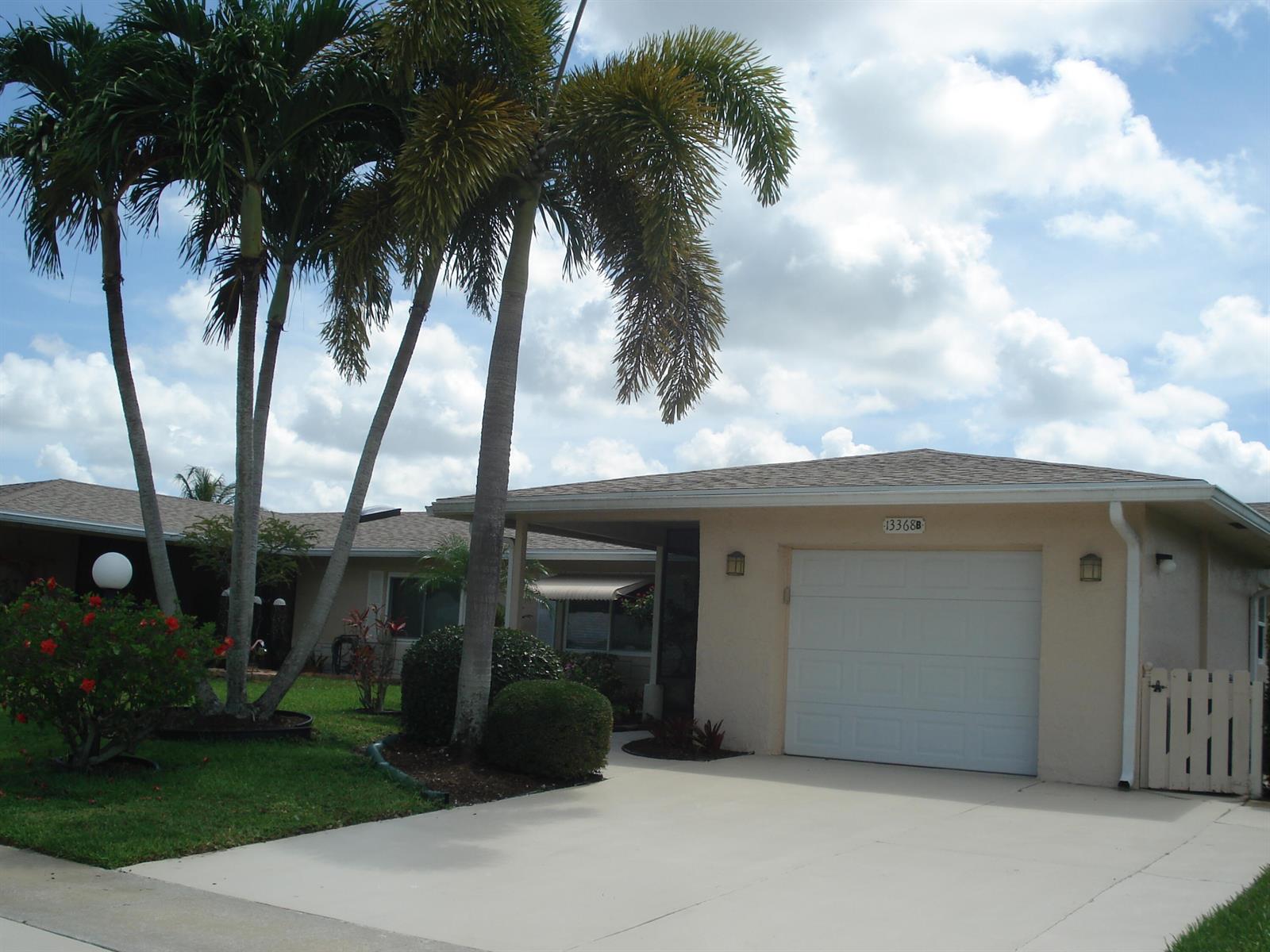 A single-story house with a white garage door, palm trees, and a green lawn — 13368 Via Vesta # B, Delray Beach FL 33484, DELRAY BEACH, FL