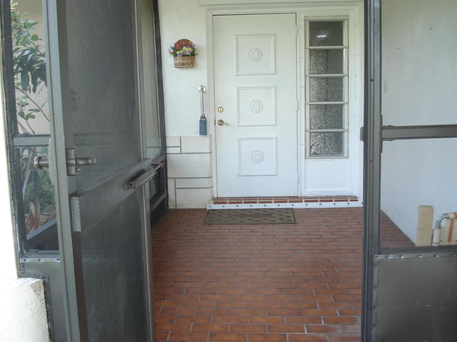 A white front door with decorative panels and a side window opens onto a brick porch — 13368 Via Vesta # B, Delray Beach FL 33484, DELRAY BEACH, FL