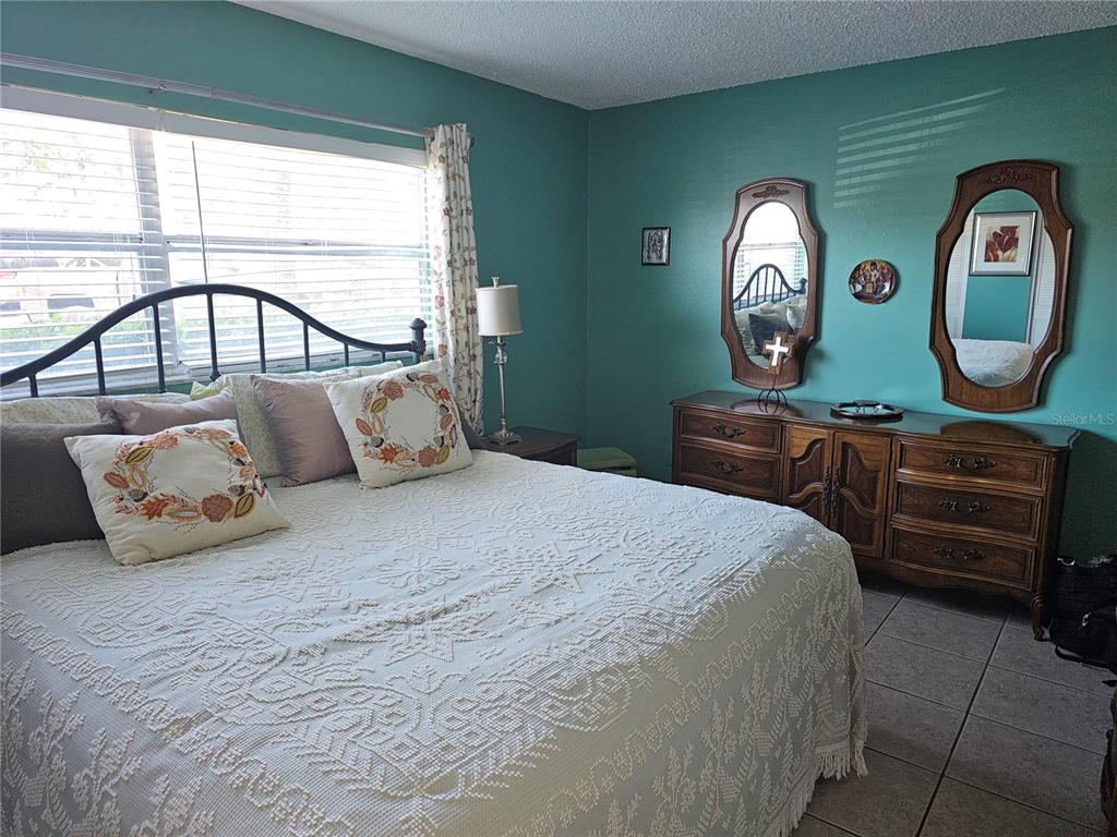 A bedroom features a bed with a white patterned spread, teal walls, and wooden furniture — 2525 W BAY DRIVE UNIT A13, BELLEAIR BLUFFS, FL
