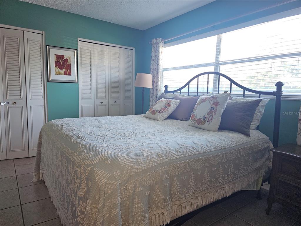 A bedroom features a bed with a textured white cover, teal walls, and louvered closet doors — 2525 W BAY DRIVE UNIT A13, BELLEAIR BLUFFS, FL