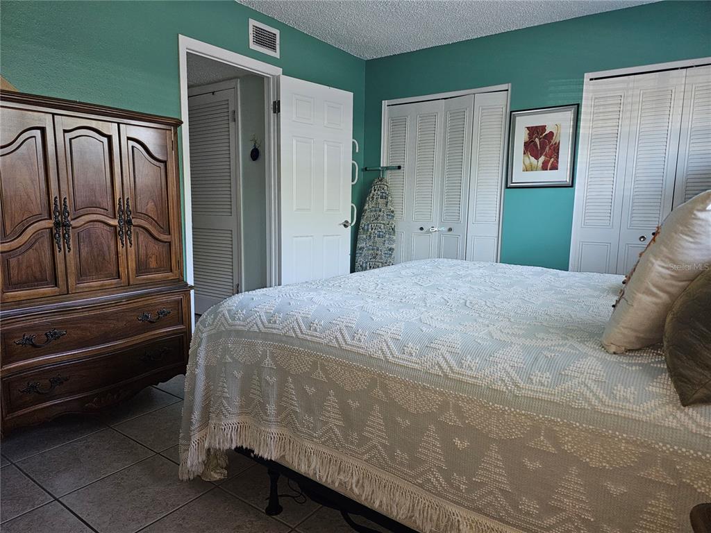 A bedroom features teal walls, a wooden armoire, a bed with a textured cover, and closets — 2525 W BAY DRIVE UNIT A13, BELLEAIR BLUFFS, FL