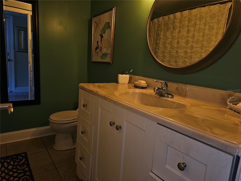 A bathroom features a white vanity with a stone countertop, a round mirror, and green walls — 2525 W BAY DRIVE UNIT A13, BELLEAIR BLUFFS, FL
