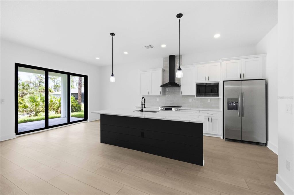 A modern kitchen features a black island, white cabinets, stainless steel appliances, and large windows — 15144 FAULKNER AVENUE, PORT CHARLOTTE, FL