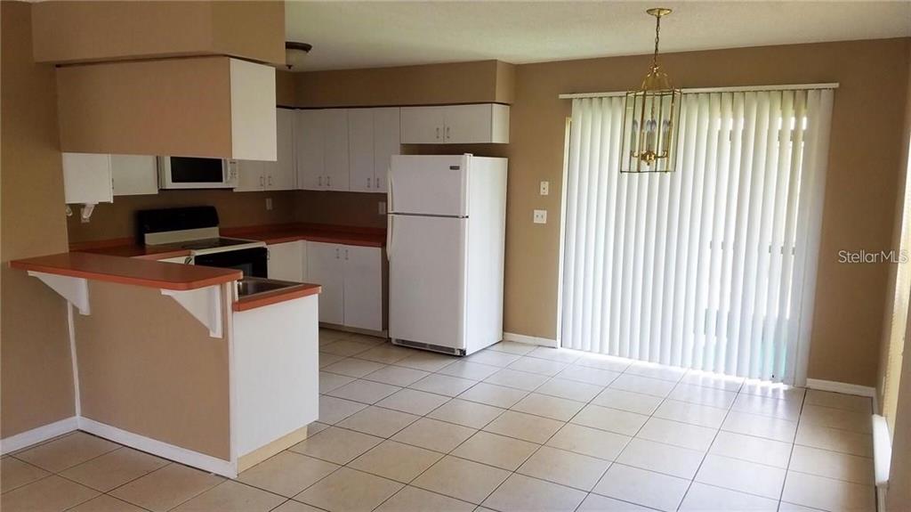 A kitchen with white cabinets, a white refrigerator, and tile flooring opens to a dining area — 132 DOUGLAS ROAD W UNIT A, OLDSMAR, FL