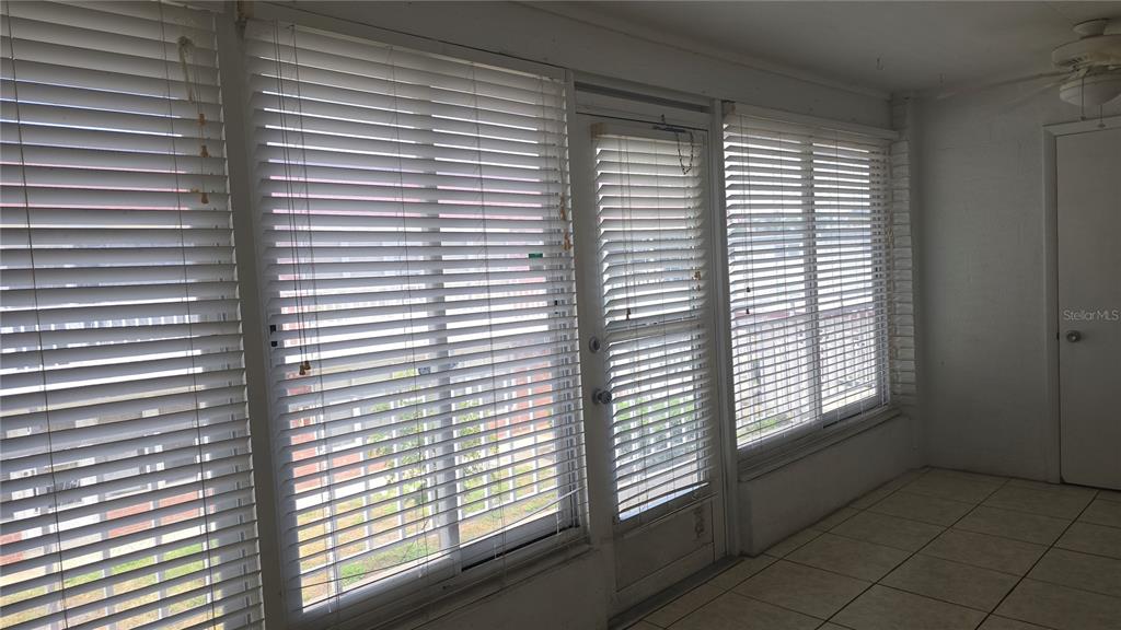 A sunroom features white tile flooring, white walls, and windows covered by horizontal blinds — 3540 32ND AVENUE N UNIT 214, ST PETERSBURG, FL