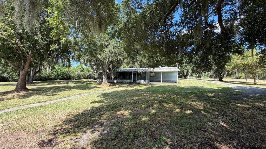 A single-story house with a screened porch sits on a large, tree-shaded grassy lot — 1324 CINDER LANE, KISSIMMEE, FL