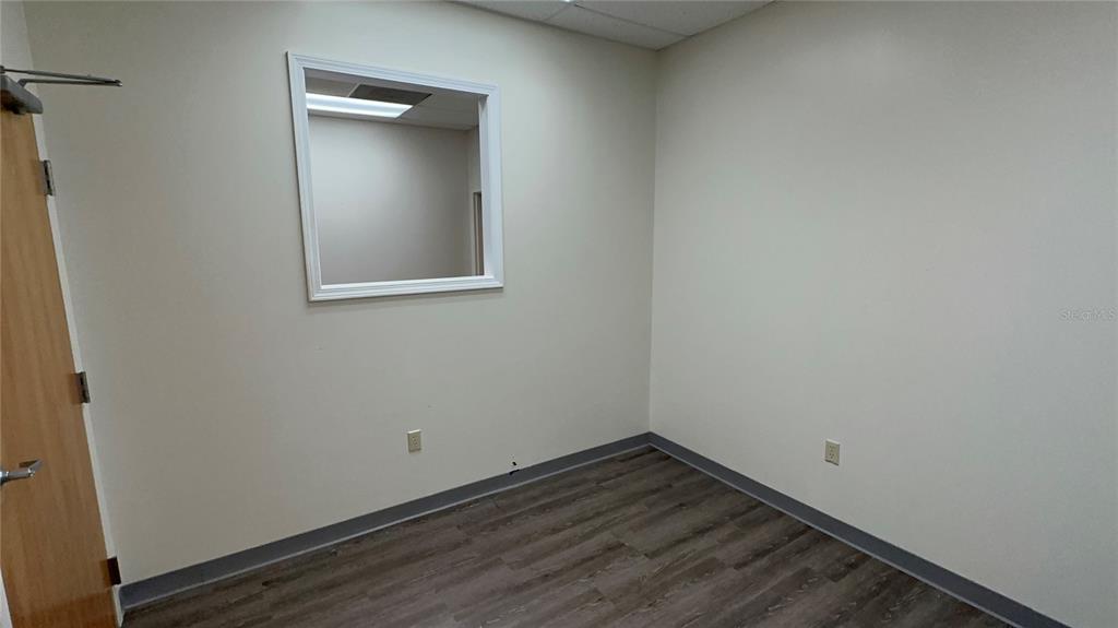 An empty office room with light walls, wood-look flooring, and a square interior window — 1534-1538 TROPIC PARK DRIVE UNIT 1534-1538, SANFORD, FL