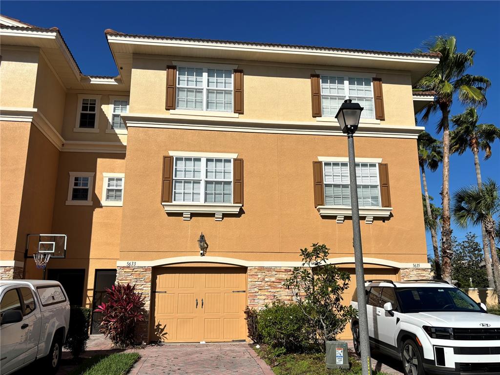 A three-story tan stucco townhouse with two garage doors and a paved driveway — 5633 BLACKFIN DRIVE, NEW PORT RICHEY, FL
