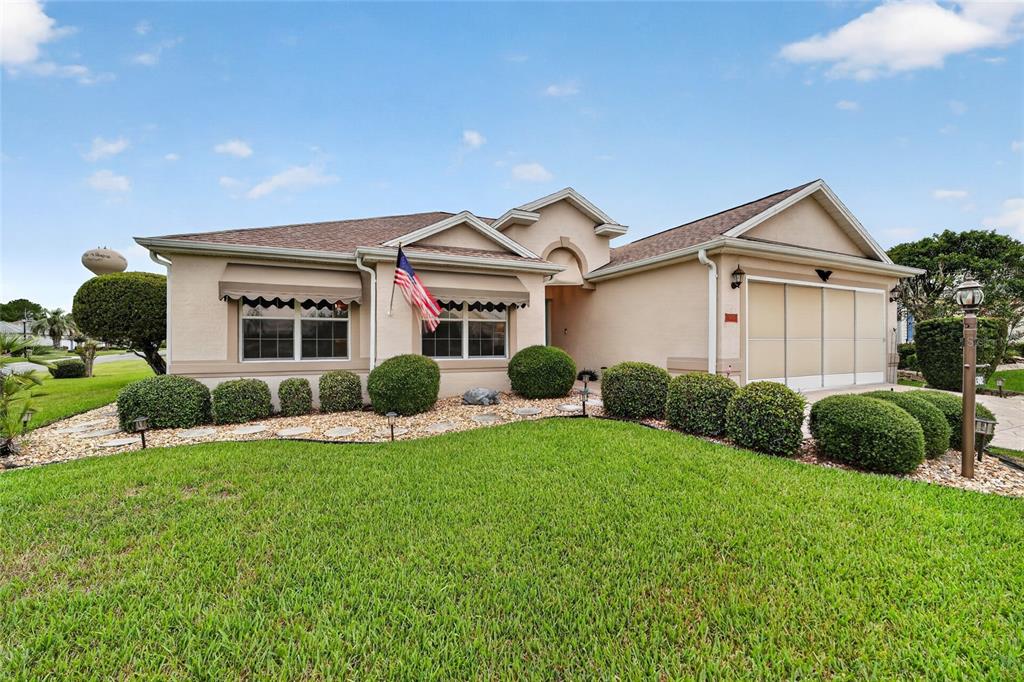 A single-story house with a beige stucco exterior, a two-car garage, and manicured landscaping — 1302 JIMENEZ COURT, THE VILLAGES, FL