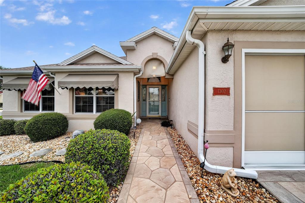 A stone walkway leads to the front entrance of a house with a beige exterior — 1302 JIMENEZ COURT, THE VILLAGES, FL