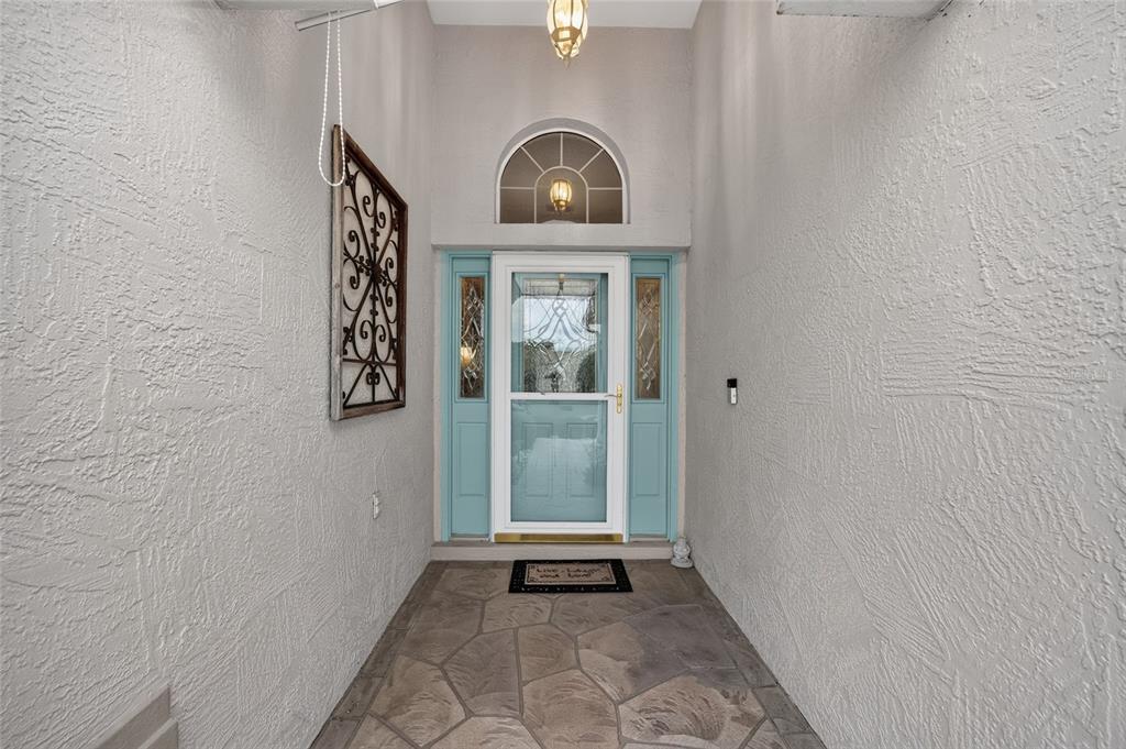 A covered entryway features a light blue front door with sidelights and stone flooring — 1302 JIMENEZ COURT, THE VILLAGES, FL