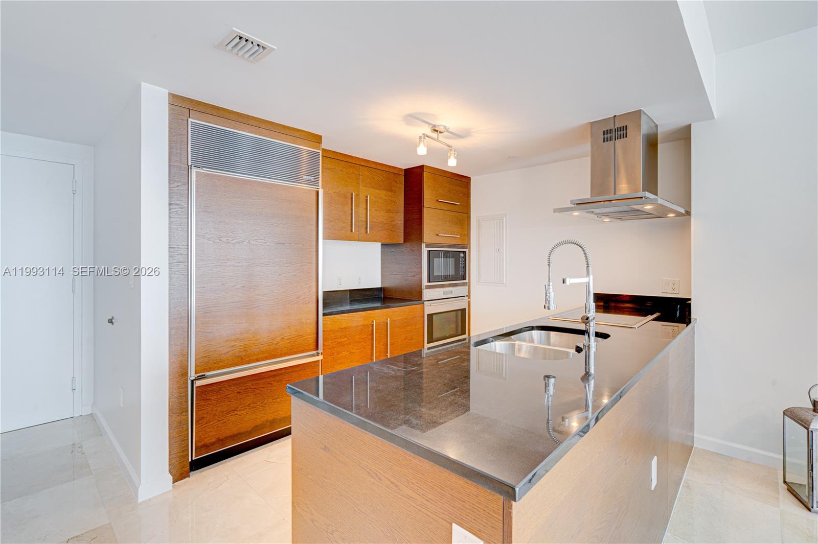 A modern kitchen features wood-paneled cabinetry, a black granite island, and stainless steel appliances — 495 Brickell Ave # 3505, Miami FL 33131, MIAMI, FL