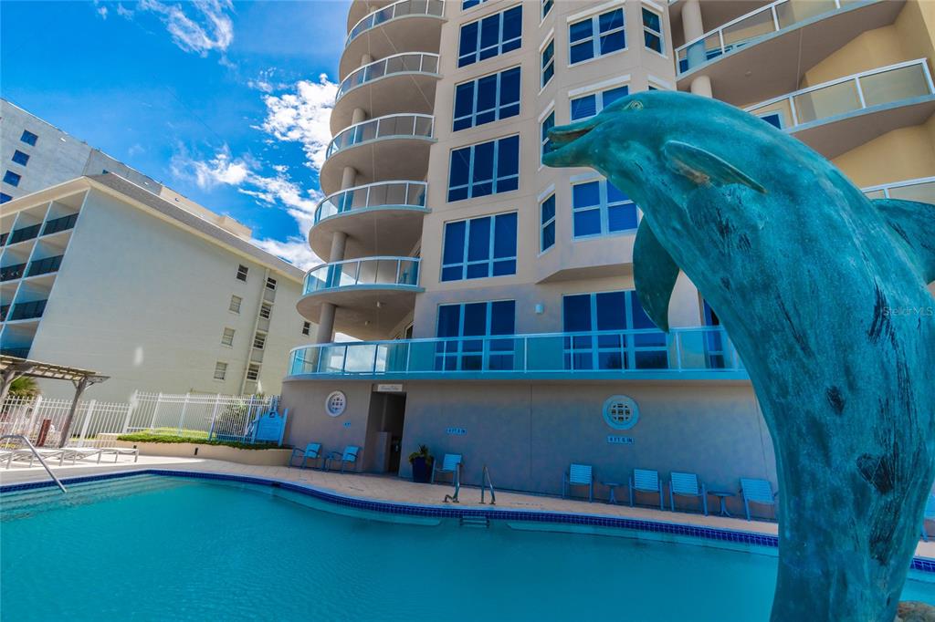 A swimming pool sits in front of a multi-story building with a large dolphin statue — 3703 S ATLANTIC AVENUE UNIT 1004, DAYTONA BEACH, FL