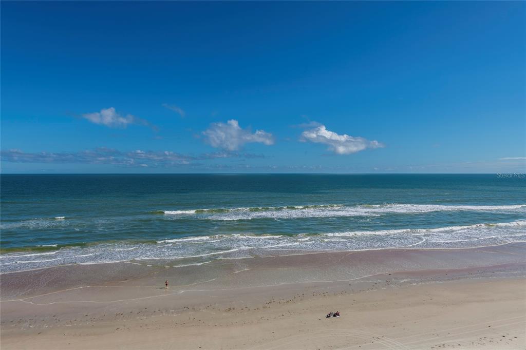 An aerial view of a sandy beach with waves meeting the shoreline under a blue sky — 3703 S ATLANTIC AVENUE UNIT 1004, DAYTONA BEACH, FL