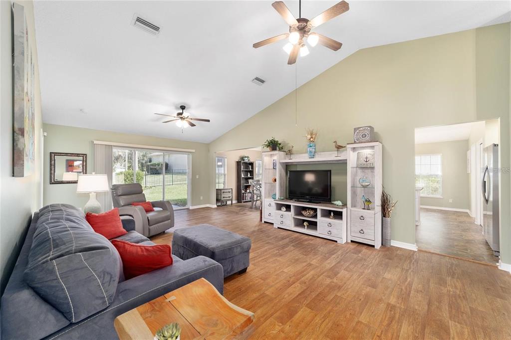 A living room with wood-look flooring, a vaulted ceiling, and a white entertainment center — 2656 SW 20TH CIRCLE, OCALA, FL
