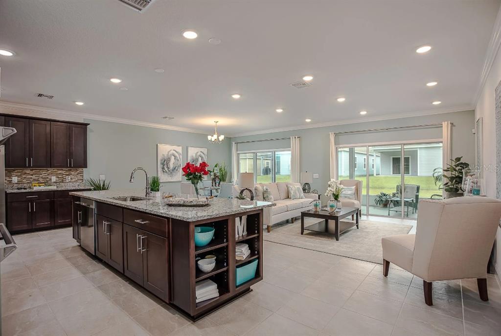 An open-concept kitchen with a large island and dark cabinets overlooks a bright living area — 3230 VICEROY COURT, POINCIANA, FL