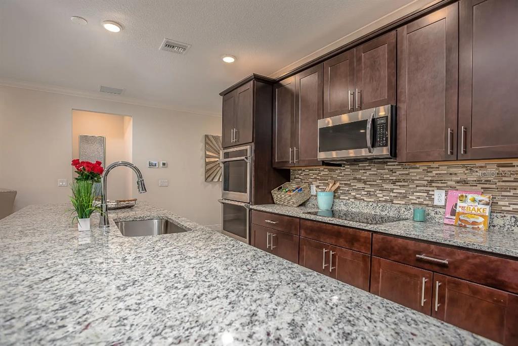 A kitchen features dark wood cabinets, granite countertops, a stainless steel microwave, and an island — 3230 VICEROY COURT, POINCIANA, FL