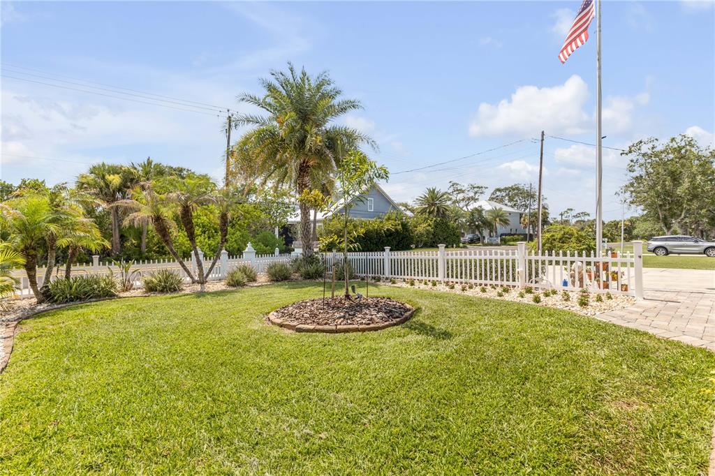 A grassy front yard features a palm tree, a small sapling, and a white fence — 521 S PENINSULA AVENUE, NEW SMYRNA BEACH, FL