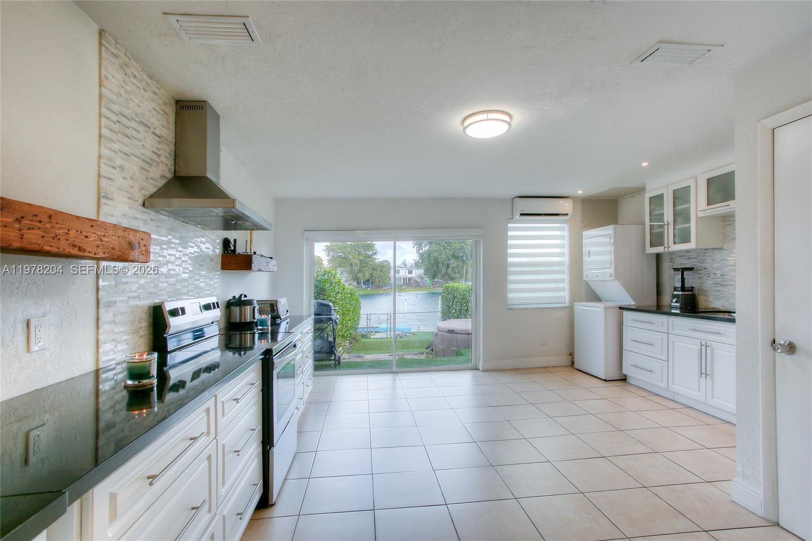 A kitchen features white cabinets, black countertops, a tiled backsplash, and a sliding glass door — 7389 W 18th Ave, Hialeah FL 33014, HIALEAH, FL