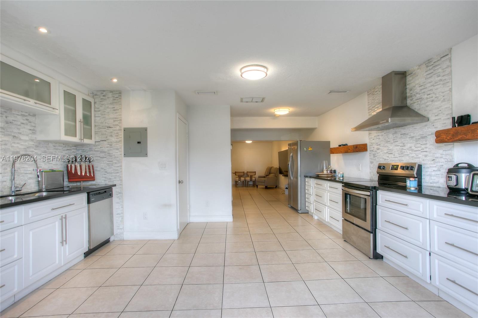 A kitchen features white cabinets, stainless steel appliances, and a tiled backsplash and floor — 7389 W 18th Ave, Hialeah FL 33014, HIALEAH, FL