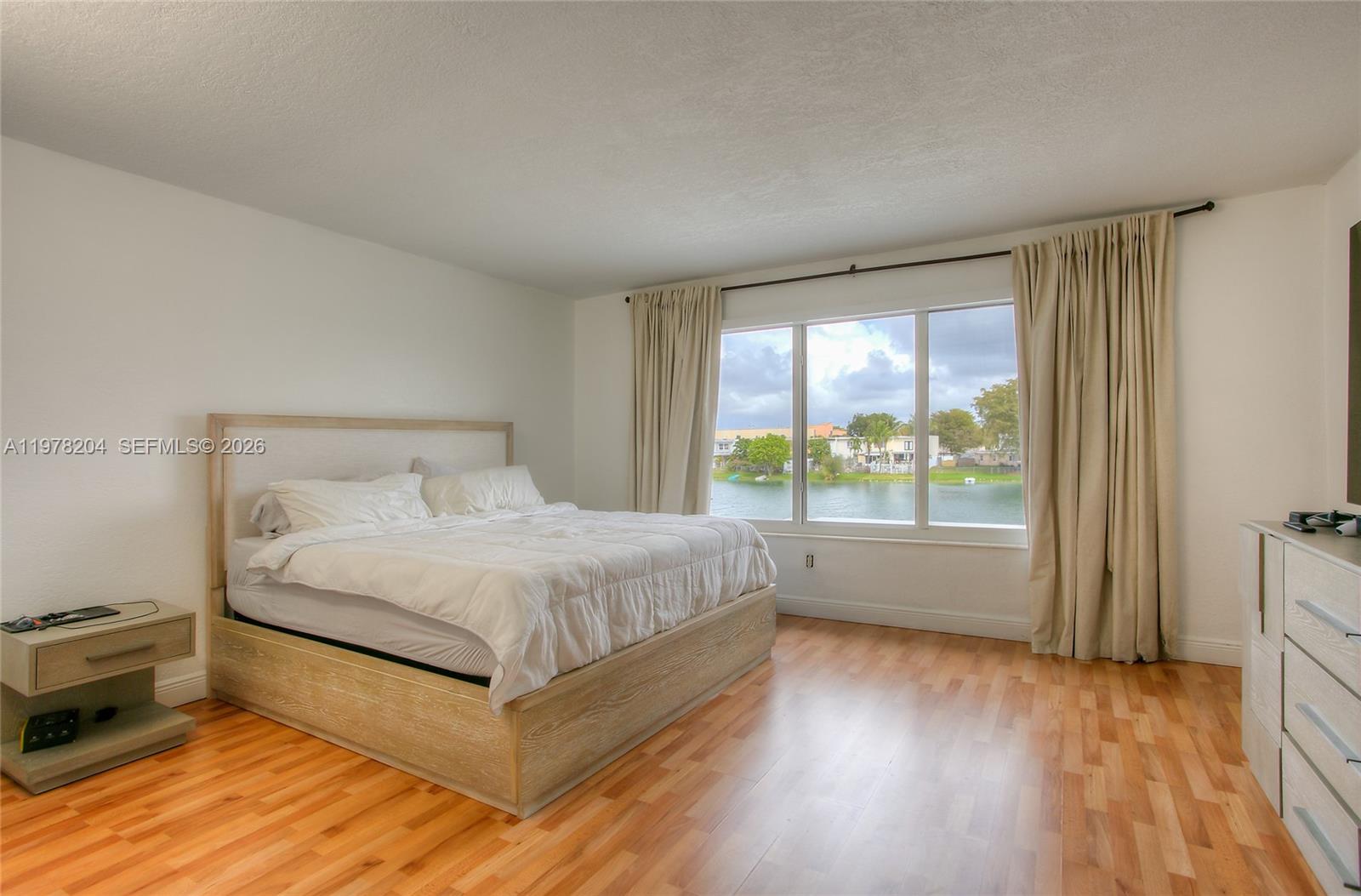A bedroom features a bed, wood flooring, and a large window overlooking a lake — 7389 W 18th Ave, Hialeah FL 33014, HIALEAH, FL